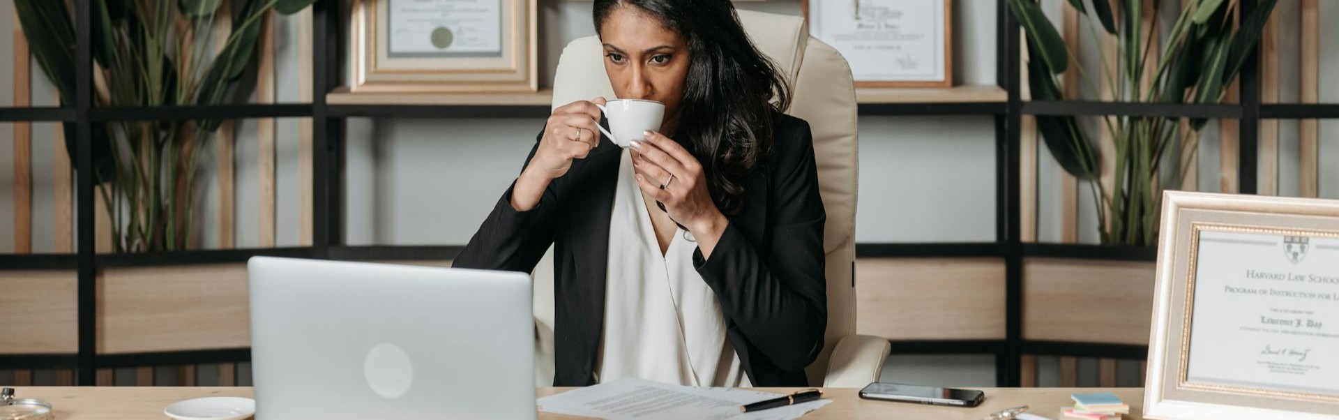 Eine Anwältin sitzt an ihrem Schreibtisch, trinkt Kaffee Rechtsanwältin trinkt am Schreibtisch Kaffee und lässt sich von Steuerberater für Rechtsanwälte beraten – steht für Mitarbeiterförderung und Personalkostenoptimierung in Anwaltskanzleien.