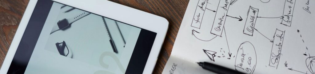 Section Image Draufsicht auf ein iPad und ein Notebook auf einem Holztisch. Auf dem iPad ist eine Präsentation geöffnet und im Notizbuch befinden sich Notizen, darüber liegt ein schwarzer Stift
