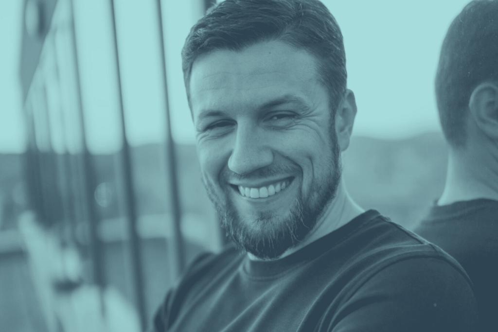 Ein lächelnder Mann mit Bart (Edin, CEO von Tean23 Steuerberatung) in türkisfarbenem Farbfilter. Das Bild wird als Titelbild für den Artikel "So findet jedes Unternehmen den passenden Steuerberater" verwendet.