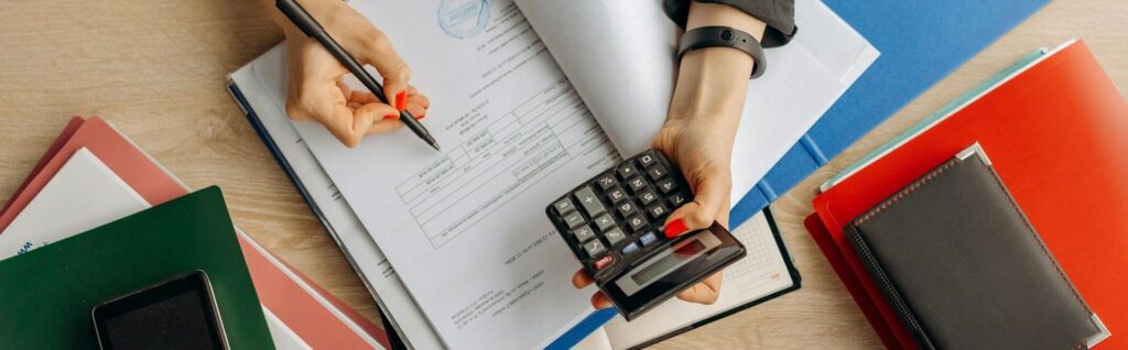 Nahaufnahme von Händen, die gleichzeitig einen Taschenrechner bedienen und in Finanzdokumenten schreiben. Das Bild visualisiert die detaillierte Berechnung der steuerlichen Vorteile einer FlexCo Österreich.