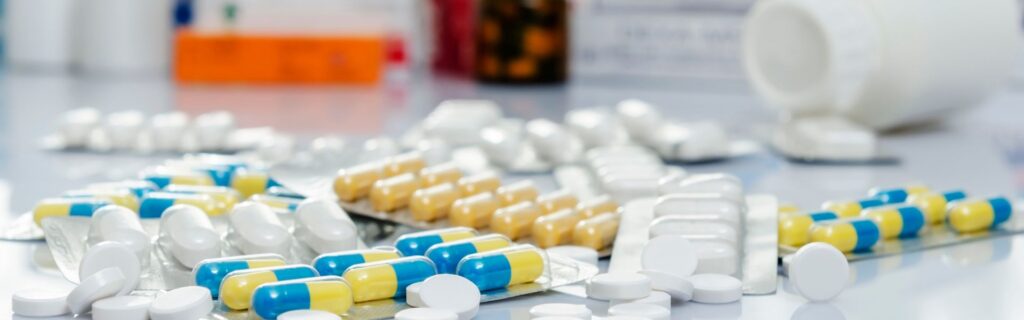 Verschiedenfarbige Medikamente und Pillen auf weißer Oberfläche mit Medikamentenbehältern im Hintergrund. Symbolisiert das Fazit zum stabilen Apothekenmanagement.