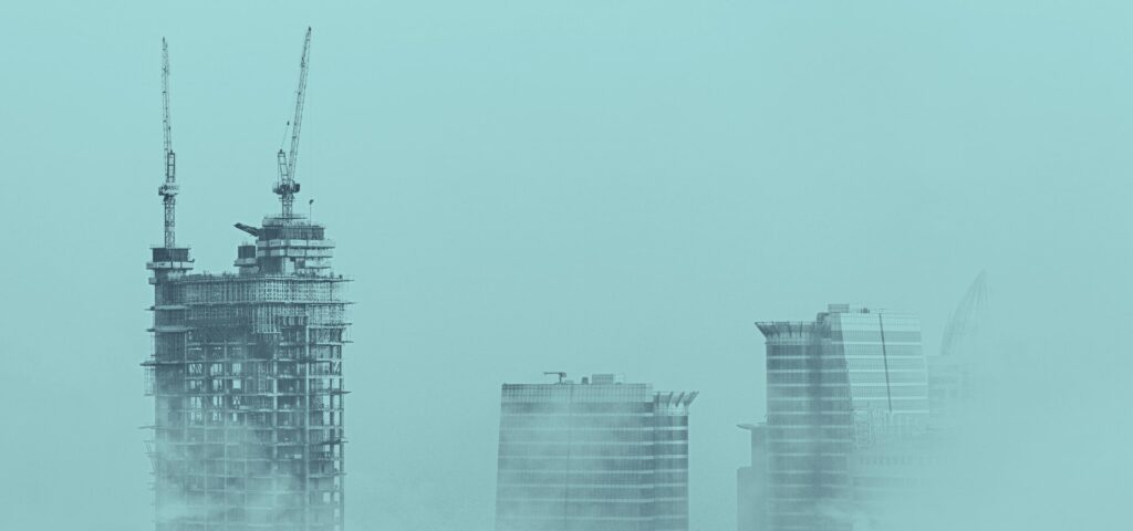 Drei Gebäude im Bau, verdeckt durch Nebel. Nur die Dächer dieser Gebäude sind sichtbar, mit Baumaschinen darauf. Die Gebäude befinden sich offensichtlich noch im Bau, da an der Außenseite noch Glas fehlt. Die Gebäude dienen als Symbol für die Wettbewerbsfähigkeit von Bauunternehmen.