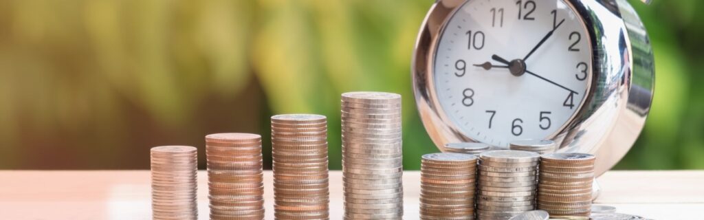 Gestapelte Münzen vor einer Uhr symbolisieren steuerliche Schwellenwerte und Zeitfaktoren beim Wechsel von Einzelunternehmer zur GmbH in Österreich