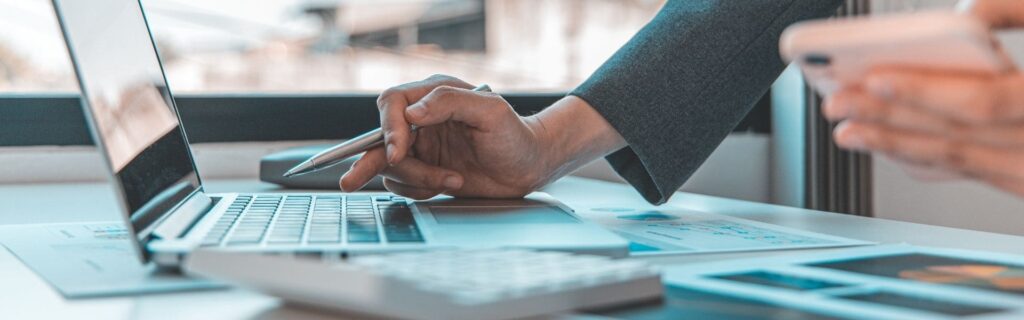 Business-Szene am Fenster mit Laptop, Smartphone und Steuerunterlagen – Person prüft Umsatzsteuer-Regeln für Online-Plattformen wie Airbnb und Etsy in Österreich