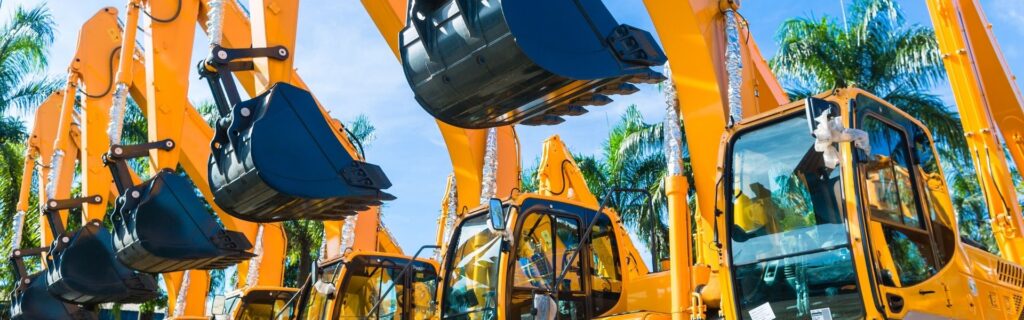 Neue, glänzende Bagger in Reihe vor Palmen und blauem Himmel – steht für den positiven Ausblick und die modernen Investitionschancen im Baugewerbe. Symbolisiert die Zukunft der Bauunternehmen durch Standort-Förderung, Digitalisierung und nachhaltige Infrastrukturprojekte.