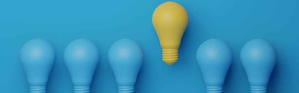 Mehrere blaue Glühbirnen stehen in einer Reihe, neben einer einzelnen gelben Glühbirne, die heraussticht. Das Bild symbolisiert innovative Beratung, kreative Lösungsansätze und den Unterschied eines wirklich guten Jahresabschlussgesprächs für Unternehmen.