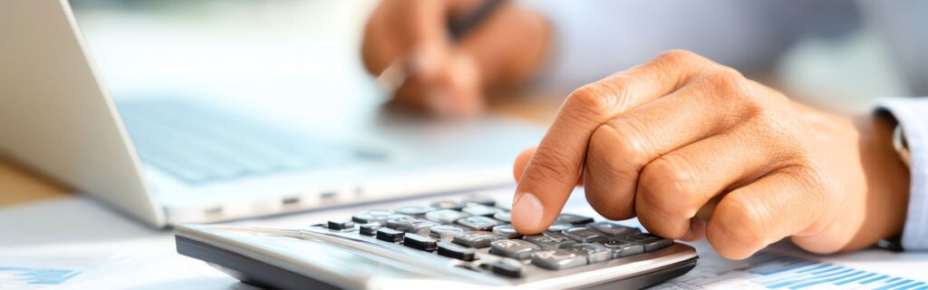 Nahaufnahme einer Hand, die Zahlen in einen Taschenrechner eingibt, im Hintergrund ein unscharfer Laptop und Dokumente. Das Bild stellt die sorgsame Berechnung der Pendlerpauschale und Pendlereuro für Arbeitgeber dar, mit Fokus auf korrekte Personalverrechnung ab 2026 und Barrierefreiheit durch klare Kontraste und Fokus auf die Fingerbewegung.