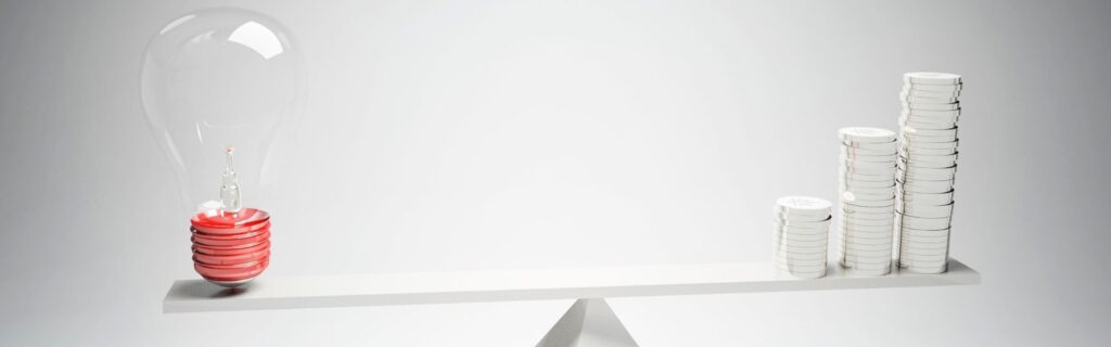 Eine große transparente Glühbirne und mehrere gestapelte Münzstapel balancieren auf einer weißen Wippe, die Gleichgewicht darstellt. Die Kombination steht symbolisch für neue steuerliche Absetzbeträge und steuerliche Vorteile für Arbeitgeber durch die Pendlerpauschale 2026 sowie Klimabonus-Änderungen in Österreich.