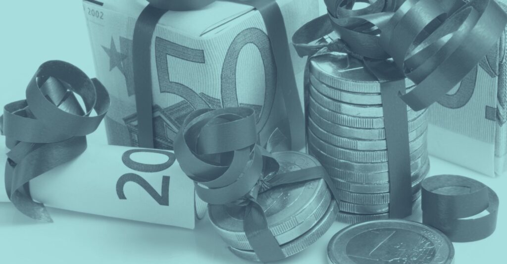 Geldscheine und Euromünzen sind mit Schleifen verziert und als Geschenk dekoriert; repräsentiert steuerfreie Sachgeschenke, Prämien und wichtige Steuertipps zu speziellen Fällen wie Krankenstand, Kündigung oder Altersteilzeit beim Weihnachtsgeld 2025.