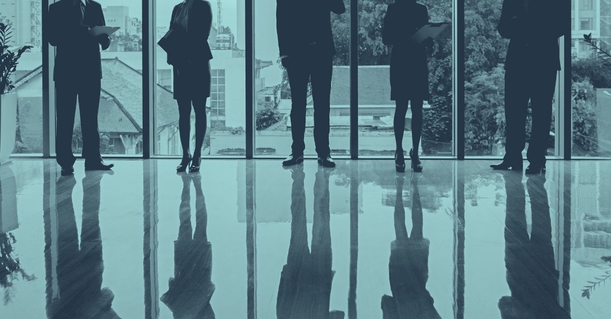 Gruppe von Unternehmern im Büro vor Panoramafenstern als Symbol für Checkliste zum Jahresende für Unternehmen.