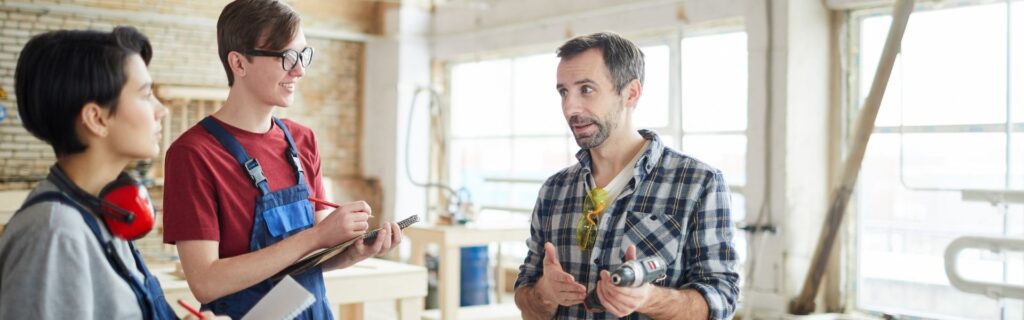 Lehrlingsausbildung im Handwerksbetrieb – Unternehmer erklärt zwei jungen Mitarbeitenden die Arbeit als strategische Antwort auf den Fachkräftemangel.