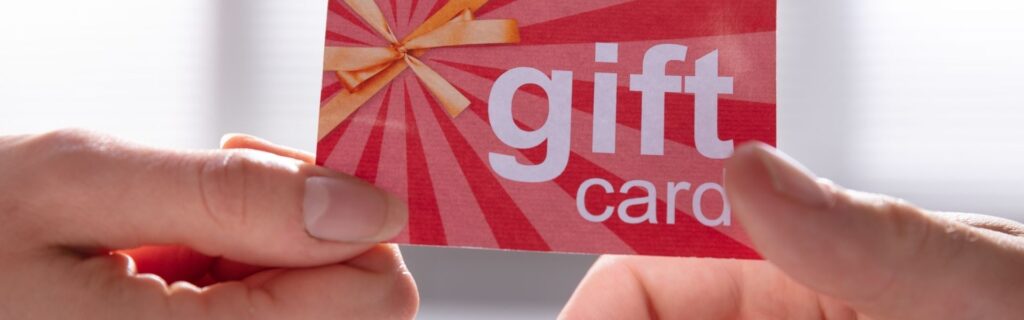 Zwei Hände halten eine rote Geschenkkarte mit goldenem Stern-Muster. Die Karte symbolisiert steuerfreie Sachbezüge und Mitarbeitergeschenke in der Personalverrechnung.