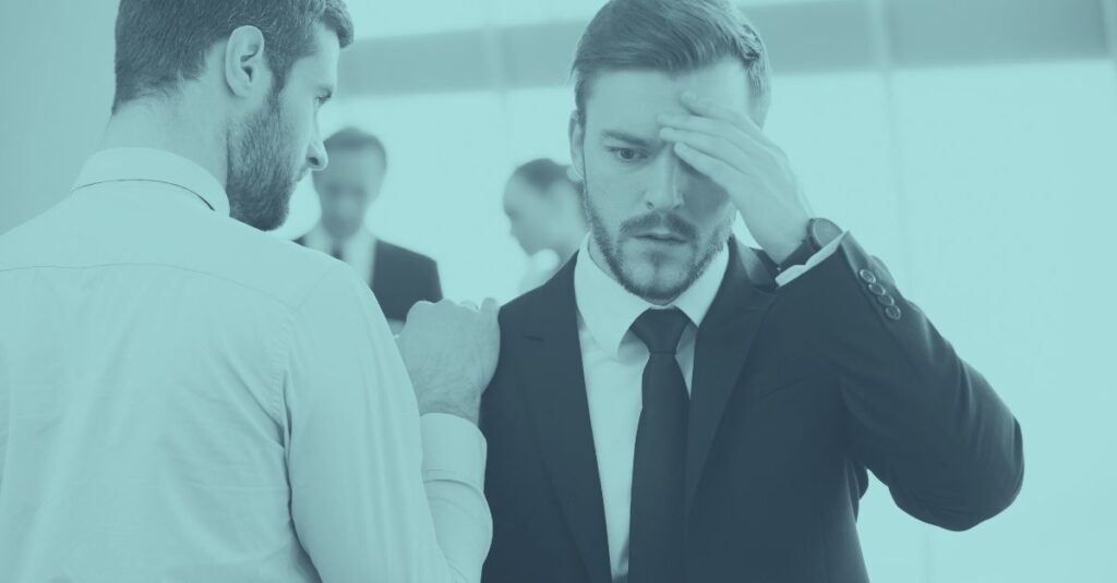 Zwei männliche Geschäftsführer stehen in einem Besprechungsraum, einer legt dem anderen die Hand auf die Schulter, während dieser nachdenklich seine Krawatte richtet – Symbolbild für heikle Gespräche über überraschende Steuerfallen für Unternehmer in Österreich.