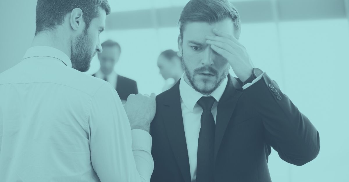 Zwei männliche Geschäftsführer stehen in einem Besprechungsraum, einer legt dem anderen die Hand auf die Schulter, während dieser nachdenklich seine Krawatte richtet – Symbolbild für heikle Gespräche über überraschende Steuerfallen für Unternehmer in Österreich.