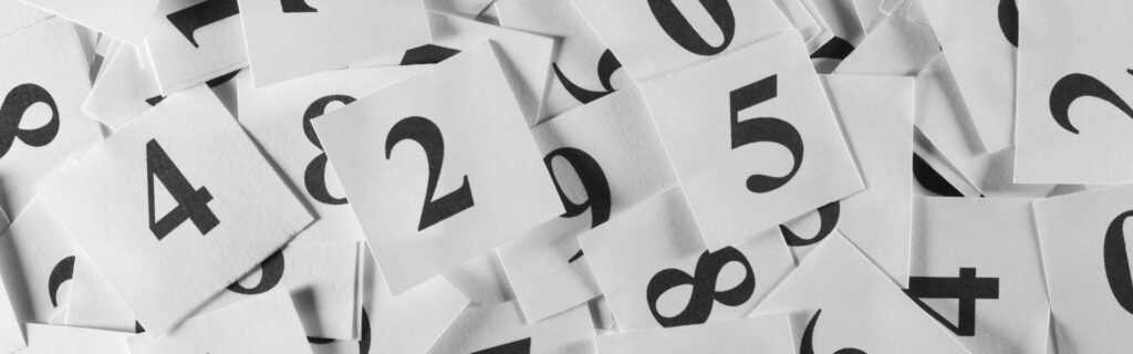 Schwarzweiße Zahlenkarten mit verschiedenen Ziffern verstreut auf weißem Untergrund – Symbolbild für wichtige Berechnungen, Umsatzgrenzen und Prozentsätze bei der Basispauschalierung 2026 in Österreich