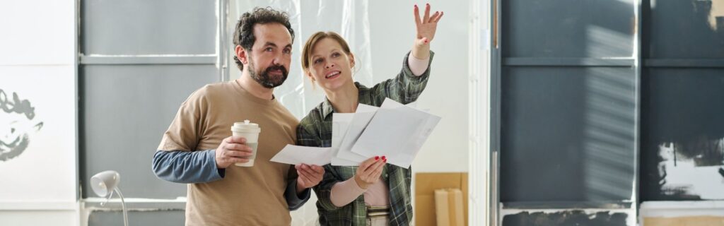 Ein Paar mit Renovierungsplänen in der Hand bespricht die Kosten einer Immobiliensanierung – Praxisbeispiel für die Planung einer 105.000 Euro Sanierung mit Sanierungsbonus, Investitionsfreibetrag und beschleunigter AfA in Österreich.
