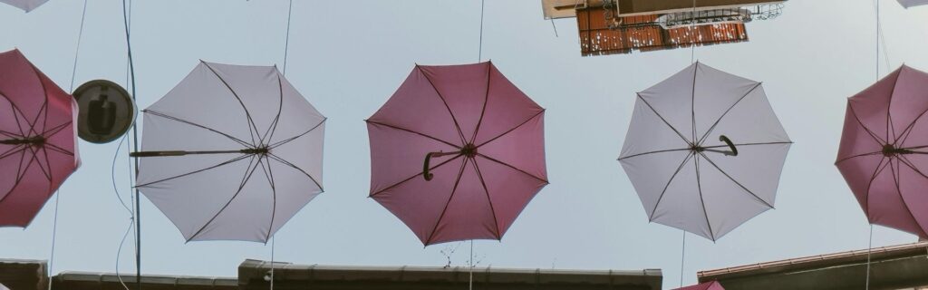 Rosa und weiße Regenschirme als Symbol für Schutzfunktion der Arbeitsplatzpauschale – was die 1.200 Euro Pauschale für Homeoffice-Kosten abdeckt und was Selbständige zusätzlich absetzen müssen.