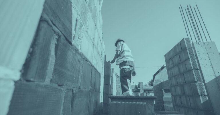 Bauarbeiter mauert eine Wand auf einer Baustelle, blaue Farbüberlagerung – Symbolbild für Betrugsbekämpfung und verschärfte Kontrollen gegen Sozialbetrug am Bau in Österreich 2026