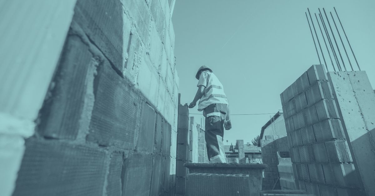Bauarbeiter mauert eine Wand auf einer Baustelle, blaue Farbüberlagerung – Symbolbild für Betrugsbekämpfung und verschärfte Kontrollen gegen Sozialbetrug am Bau in Österreich 2026