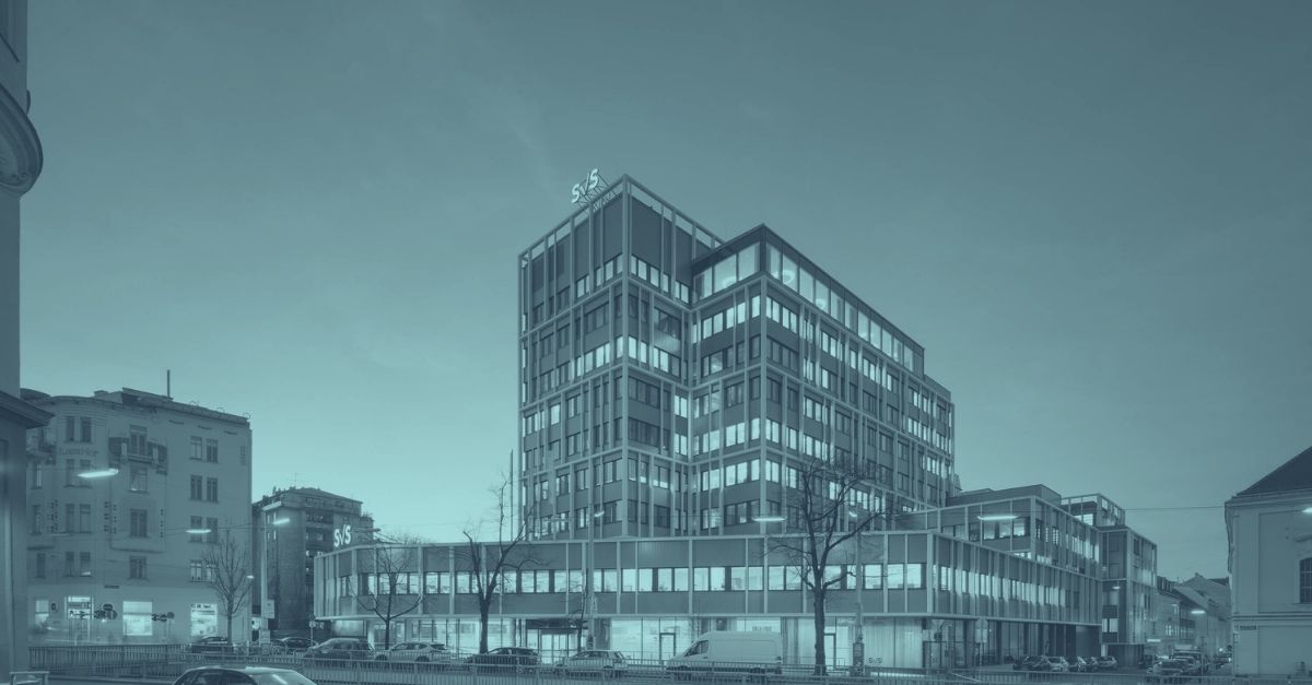 SVS-Beiträge 2026: Hauptgebäude der Sozialversicherung der Selbständigen (SVS) in Wien bei Dämmerung. Moderner neunstöckiger Bürokomplex mit Glasfassade und beleuchteten Fenstern in türkis-blauem Licht. SVS-Logo an Gebäudespitze. Symbolbild für SVS-Beitragsgrundlage, Sozialversicherung Selbständige und Gewinnfreibetrag-Optimierung 2026 in Österreich.