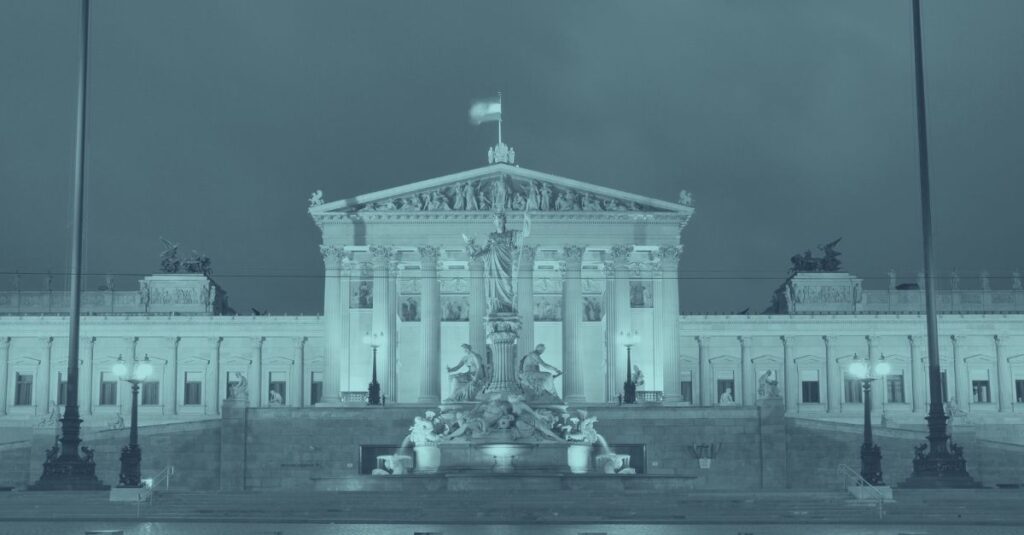 Österreichisches Parlamentsgebäude in Wien bei Nacht beleuchtet in Türkis-Tönen, symbolisiert Wirtschaftslage Österreich 2026 und Rezessionsprognose. Parlamentsfassade mit Athena-Brunnen im Vordergrund repräsentiert politische und wirtschaftliche Stabilität nach zwei Jahren Rezession. Titelbild zum Blog über WIFO Wirtschaftsprognose, BIP-Wachstum, Inflation und Branchenentwicklung für KMU, Bau und Gesundheitssektor.