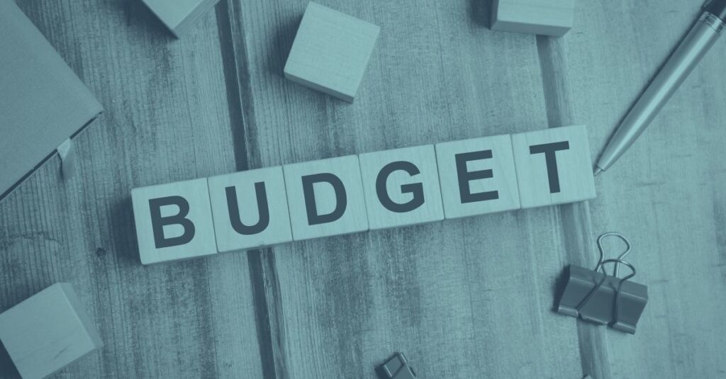 Holzwürfel mit dem Schriftzug BUDGET auf einem Holztisch, umgeben von Büroklammern und einem Stift, mit blauer Farbüberlagerung – Symbolbild für die österreichische Budgetkrise und die Rückkehr der kalten Progression 2026