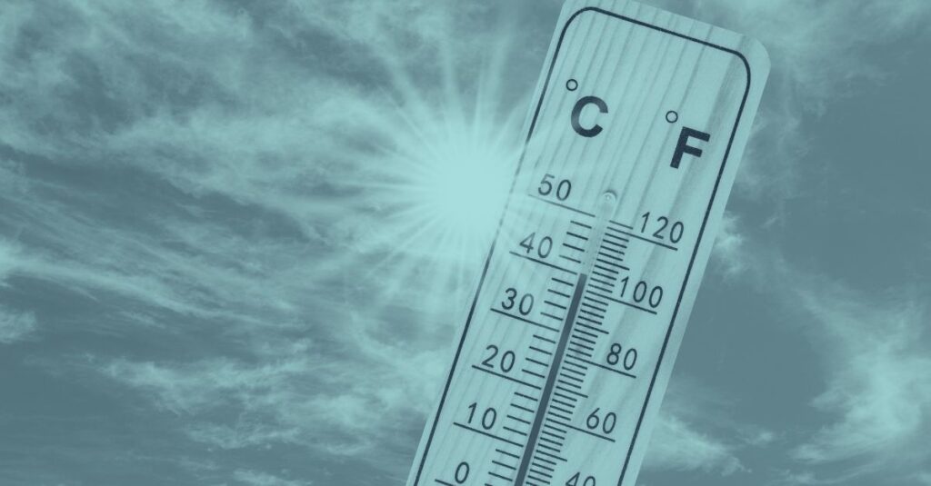 Holzthermometer mit hohen Temperaturen vor sonnigem Himmel – Symbol für Sommerhitze und Hitzeschutz am Arbeitsplatz im Freien gemäß Hitzeschutzverordnung 2026.