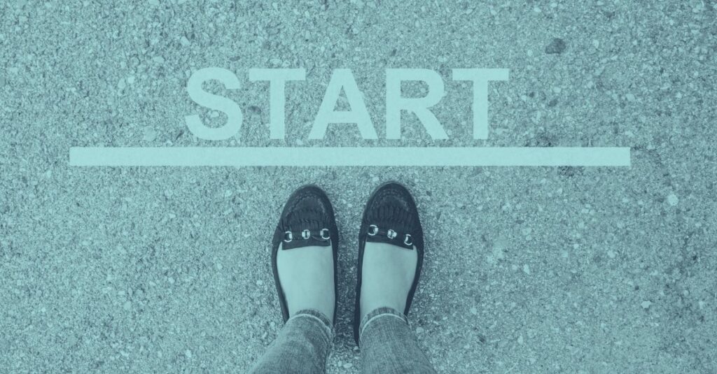 Zwei Füße in flachen Schuhen stehen an einer weißen Startlinie mit dem Wort START auf Asphalt, als Symbol für den Einstieg in das Thema Reisekosten und Spesenabrechnung 2026 in Österreich mit Taggeld, Kilometergeld und Dienstreisen.