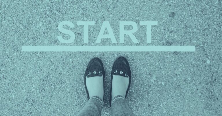 Zwei Füße in flachen Schuhen stehen an einer weißen Startlinie mit dem Wort START auf Asphalt, als Symbol für den Einstieg in das Thema Reisekosten und Spesenabrechnung 2026 in Österreich mit Taggeld, Kilometergeld und Dienstreisen.
