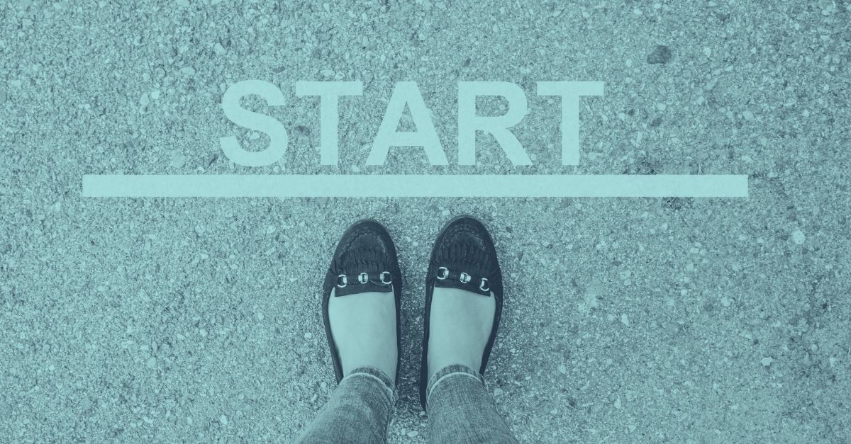 Zwei Füße in flachen Schuhen stehen an einer weißen Startlinie mit dem Wort START auf Asphalt, als Symbol für den Einstieg in das Thema Reisekosten und Spesenabrechnung 2026 in Österreich mit Taggeld, Kilometergeld und Dienstreisen.