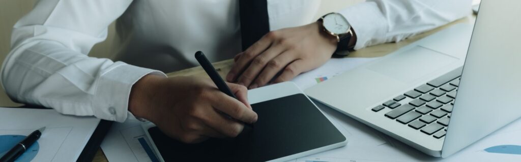 Person im weißen Hemd analysiert Unterlagen neben einem Laptop und schreibt mit einem digitalen Stift – symbolisch dafür, dass Arbeitgeber die neue Trinkgeldregelung in Österreich 2026 prüfen, ihre Zahlen durchgehen und die nächsten Schritte für die Anpassung der Lohnverrechnung planen.