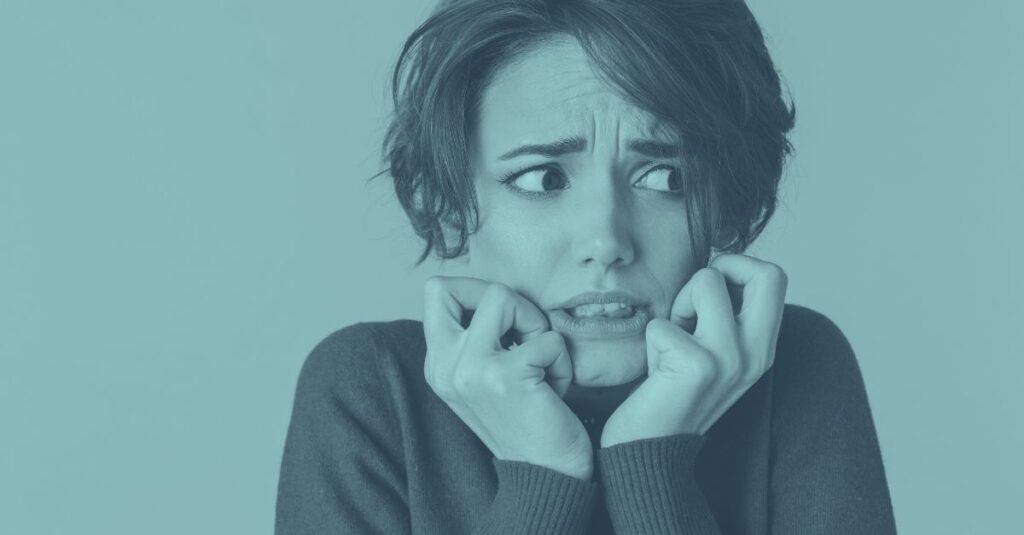 Eine junge Frau blickt besorgt zur Seite und beißt sich auf die Lippen, auf blauem Hintergrund. Symbolbild für die Angst vor unerwarteten SVS-Nachzahlungen und der Nachbemessung von Sozialversicherungsbeiträgen für Selbständige in Österreich.