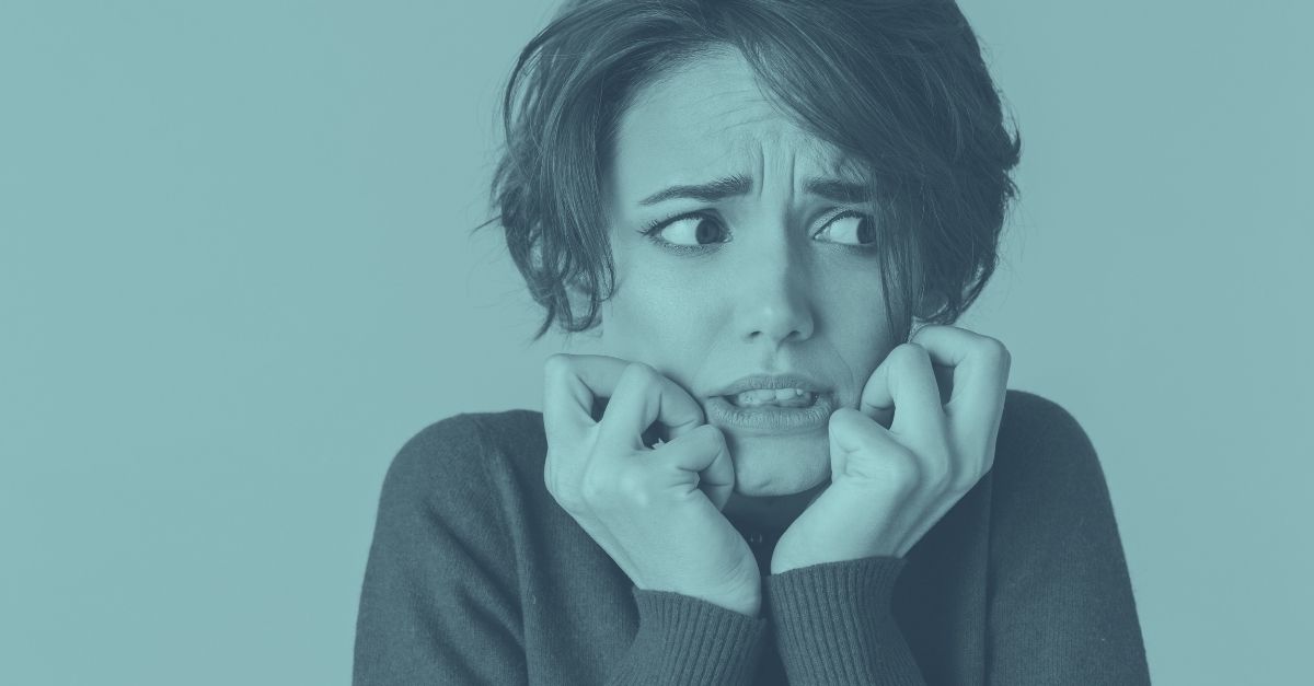 Eine junge Frau blickt besorgt zur Seite und beißt sich auf die Lippen, auf blauem Hintergrund. Symbolbild für die Angst vor unerwarteten SVS-Nachzahlungen und der Nachbemessung von Sozialversicherungsbeiträgen für Selbständige in Österreich.