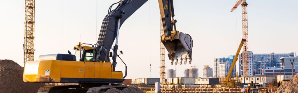 Großbaustelle mit Bagger und Kränen vor Stadtkulisse – Symbolbild für Betrugsbekämpfung am Bau, Subunternehmer-Haftung und neue Risiken durch die Budgetsanierung 2026