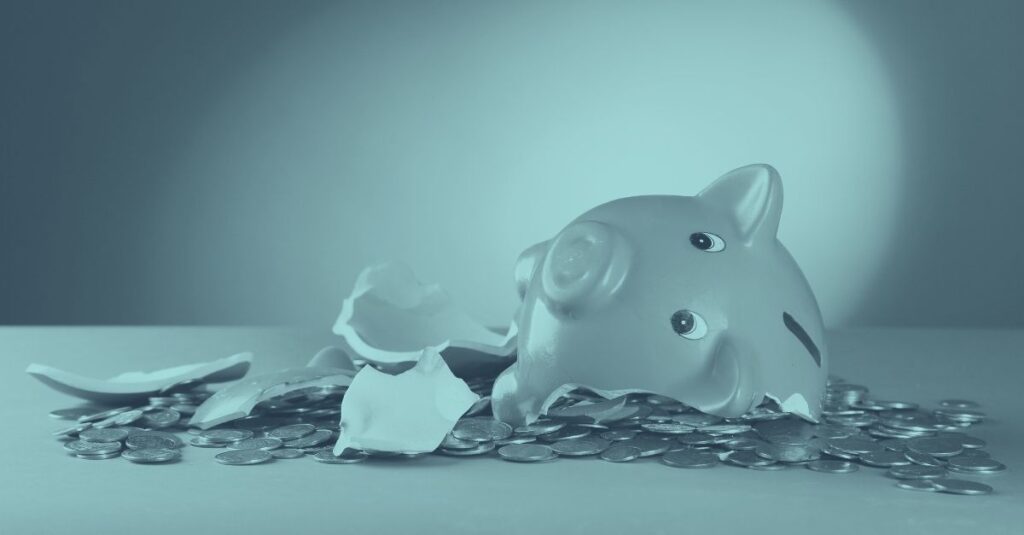 Ein in Stücke zerbrochenes rosa Sparschwein liegt auf einem großen Haufen von Geldmünzen vor einem blaugrauen Hintergrund. Das Bild symbolisiert die finanzielle Belastung für Unternehmen, die mit einer COFAG Rückforderung oder der Rückzahlung von Corona-Förderungen konfrontiert sind.