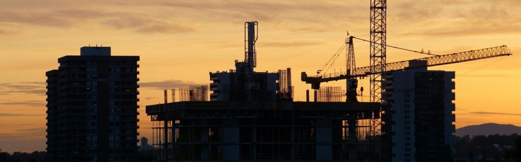 Baustelle bei Sonnenuntergang mit Baukränen und Rohbau als Bild zur BUAK im Baugewerbe; passend zu Urlaubs-, Abfertigungs- und Zuschlagsverrechnung für Bauunternehmen in Österreich.