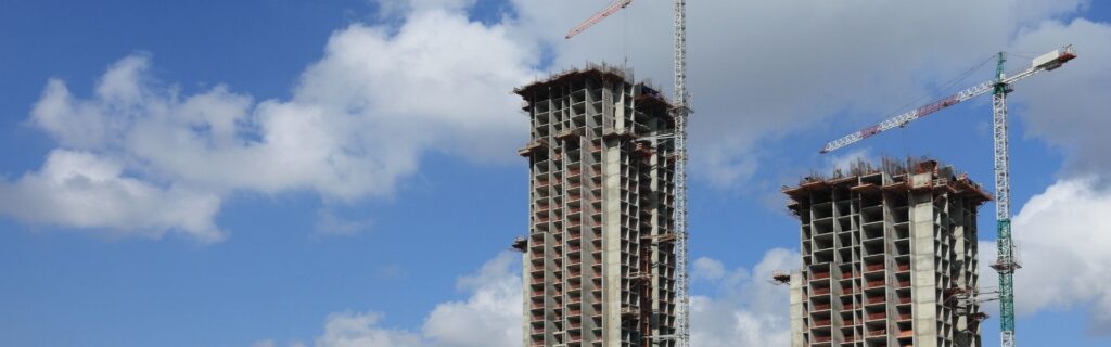 Mehrere Wolkenkratzer im Rohbau mit sichtbaren Betonstrukturen, Stockwerksnummerierung und Baukränen, Symbolbild für rückläufige Bauvolumina im Hochbau und Neubau in Österreich