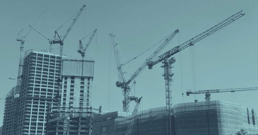 Baustelle mit mehreren im Rohbau befindlichen Hochhäusern und zwei Baukränen vor blauem Himmel mit Wolken, Symbolbild für die Bauwirtschaft Österreich 2026 und aktuelle Zahlen zur Baukonjunktur