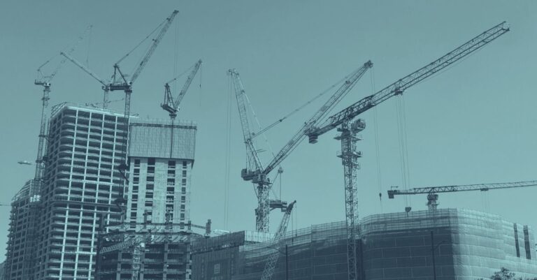 Baustelle mit mehreren im Rohbau befindlichen Hochhäusern und zwei Baukränen vor blauem Himmel mit Wolken, Symbolbild für die Bauwirtschaft Österreich 2026 und aktuelle Zahlen zur Baukonjunktur
