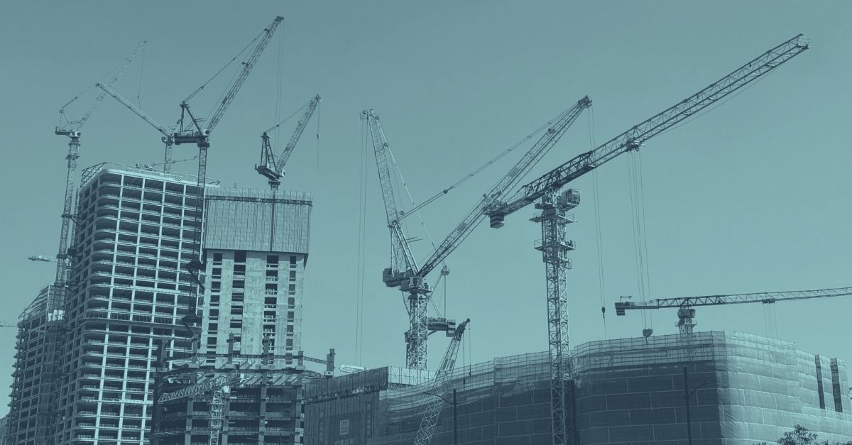 Baustelle mit mehreren im Rohbau befindlichen Hochhäusern und zwei Baukränen vor blauem Himmel mit Wolken, Symbolbild für die Bauwirtschaft Österreich 2026 und aktuelle Zahlen zur Baukonjunktur