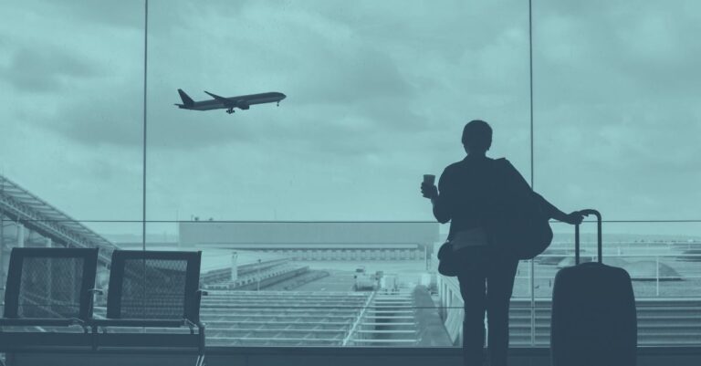 Person mit Koffer blickt im Flughafen durch ein Fenster auf ein startendes Flugzeug. Symbolfoto für grenzüberschreitende Entsendung nach Österreich, Dienstreisen und die Bedeutung der A1 Bescheinigung für die Sozialversicherung von entsandten Mitarbeitern.