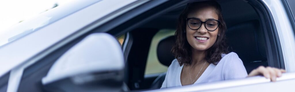 Frau sitzt am Steuer eines Elektroautos und blickt aus dem geöffneten Fahrerfenster, symbolisch für die private Nutzung eines E-Firmenwagens und den halben Sachbezug